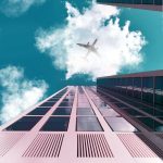 A plane flying over tall skyscrapers with a clear sky and clouds.