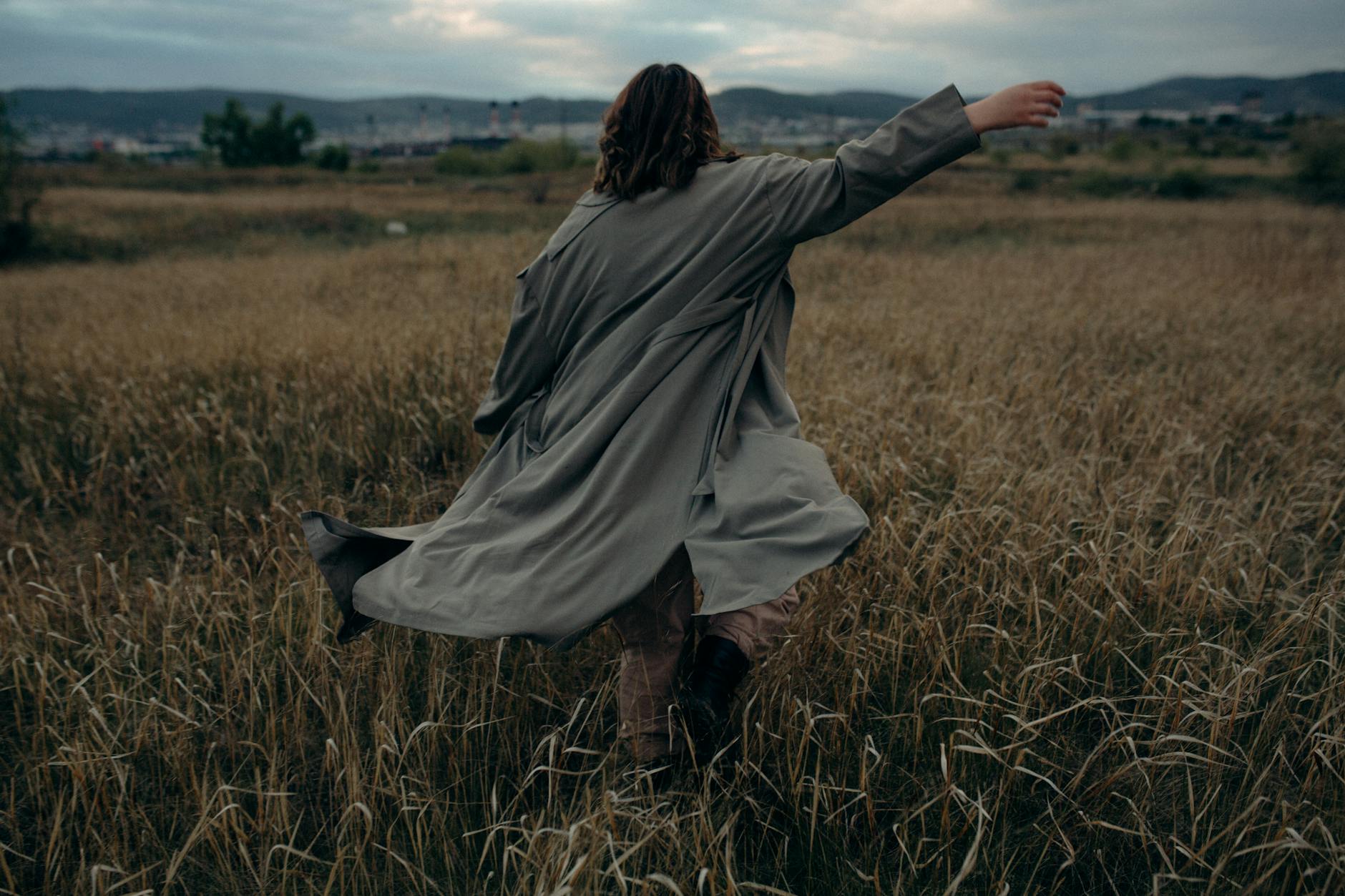 A person in a coat walking through a rural grassy field at dusk, showing a sense of freedom and solitude.