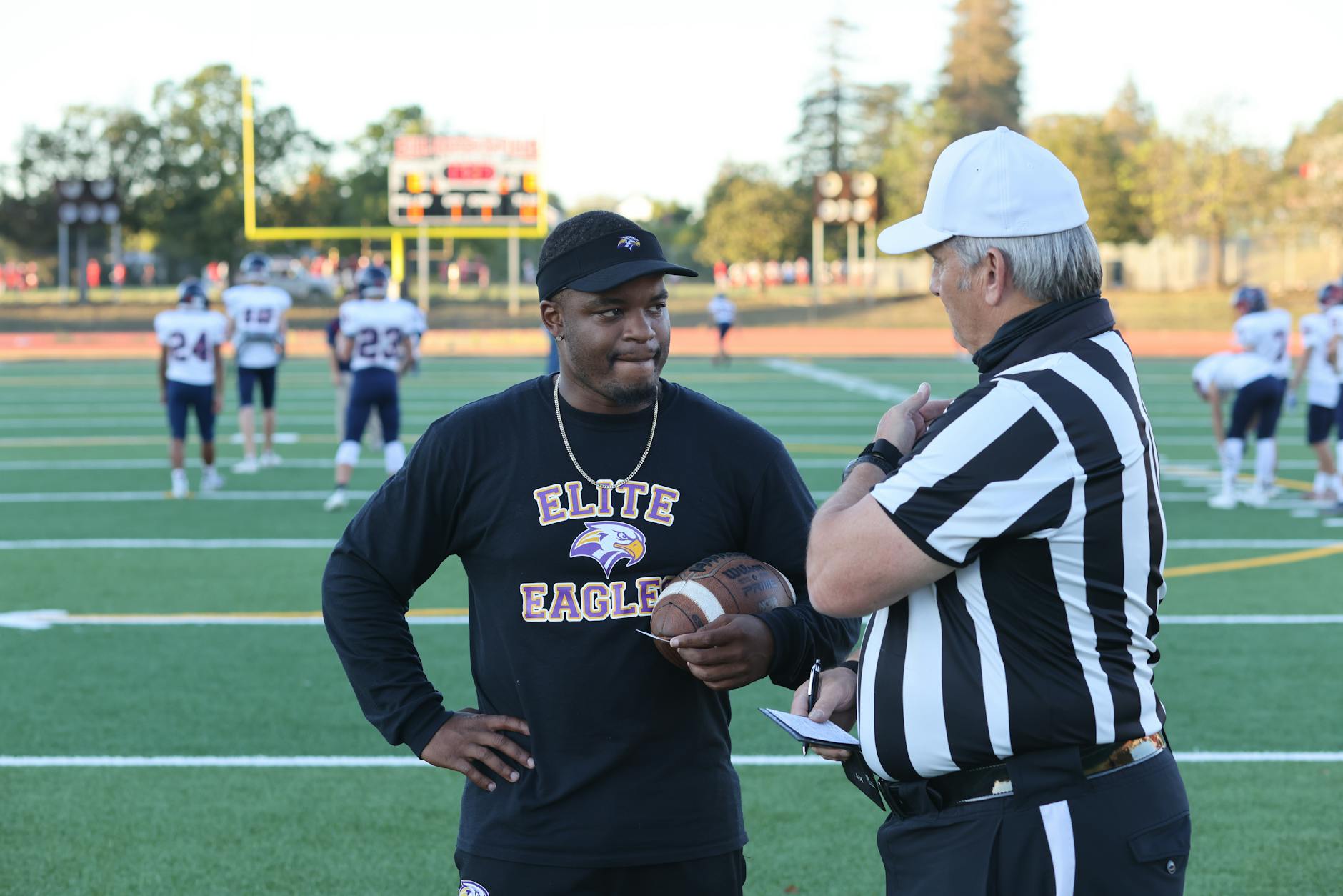 A referee and a football coach discuss the game strategy on the field.