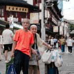 Two elderly men carry shopping bags along a bustling urban street, embodying a vibrant city life scene.