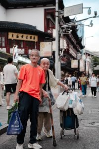 Two elderly men carry shopping bags along a bustling urban street, embodying a vibrant city life scene.