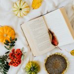Overhead view of autumn leaves, pumpkins, and open book creating seasonal ambiance.