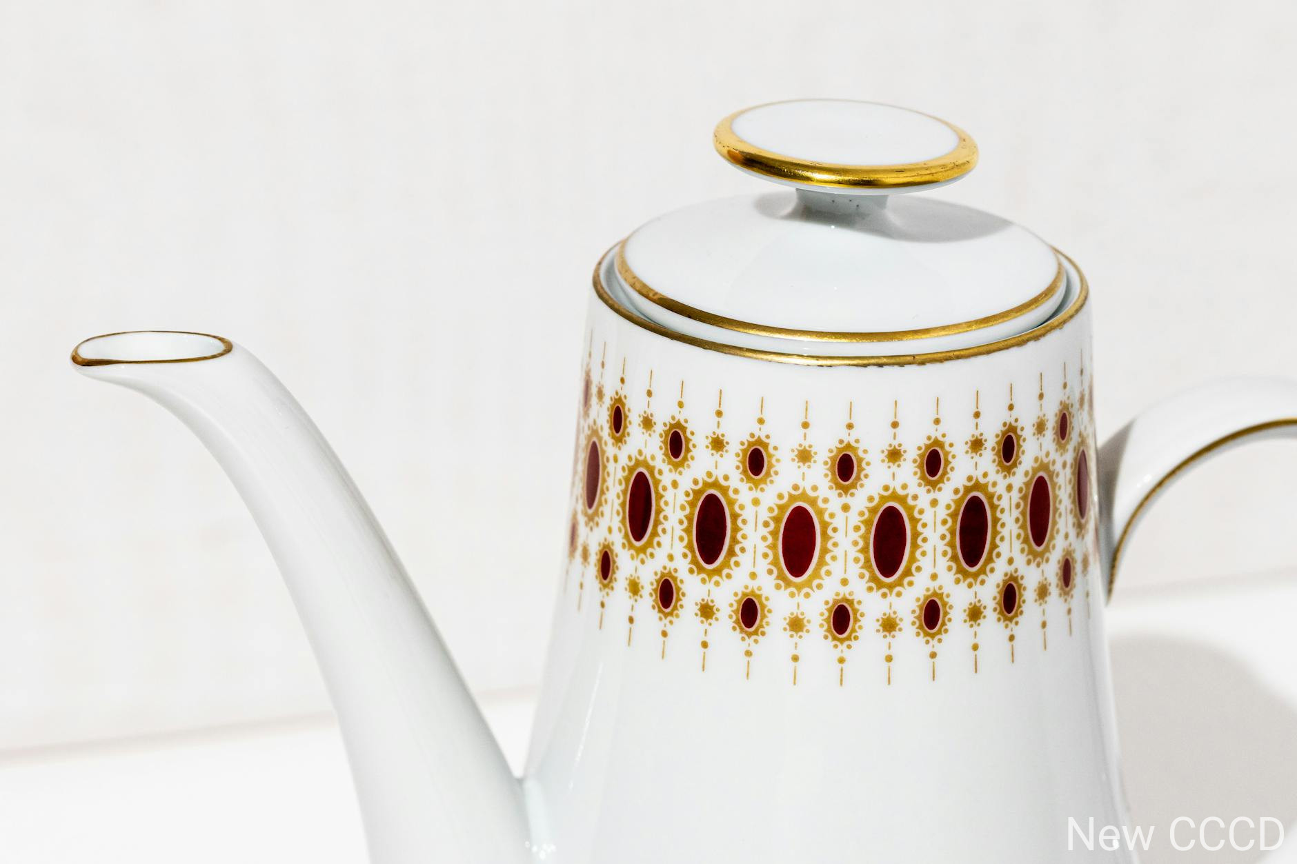 A stylish white porcelain teapot featuring intricate gold and red designs, ideal for tea-time elegance.